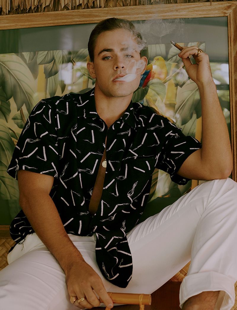 Smoking a cigar, Dacre Montgomery sports an AMIRI shirt with Ralph Lauren pants.