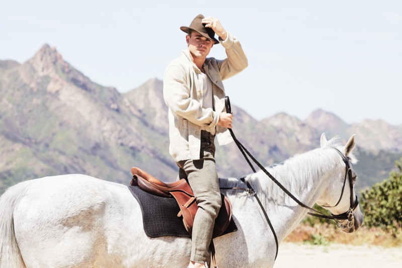 Riding a horse, Dacre Montgomery sports an Our Legacy linen jacket, Billy tank, Man 1924 trousers, and Golden Goose sneakers.