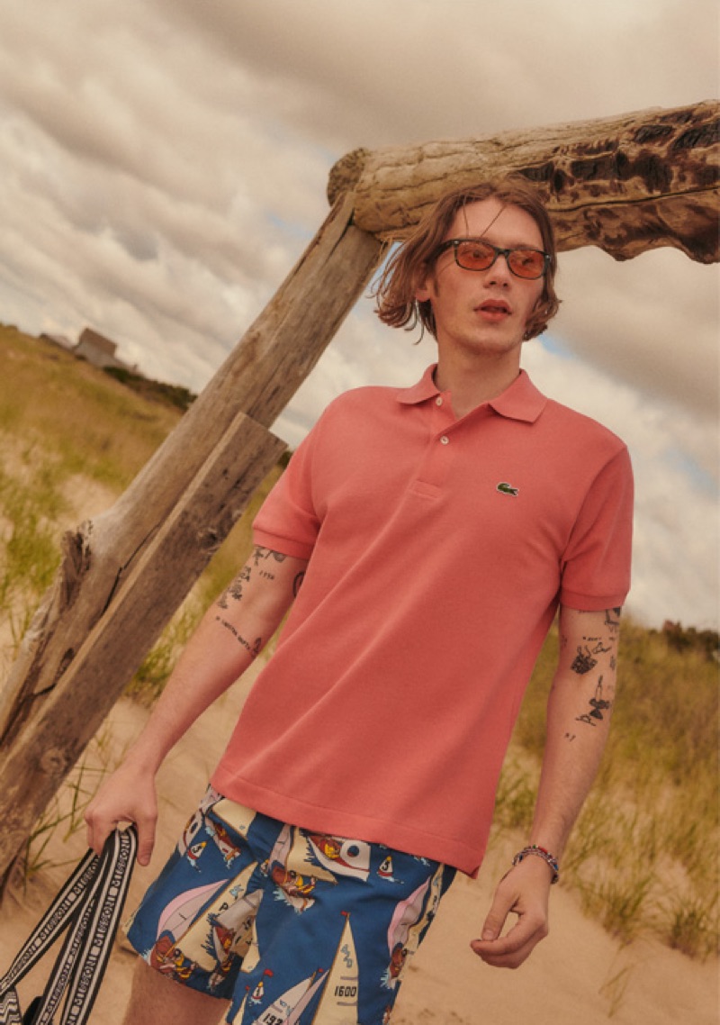 Taking to the beach, Luca Bertea wears a Lacoste polo, Bather trunks, and Ray-Ban New Wayfarer sunglasses. He also dons bracelets by Scoscha and Mikia.
