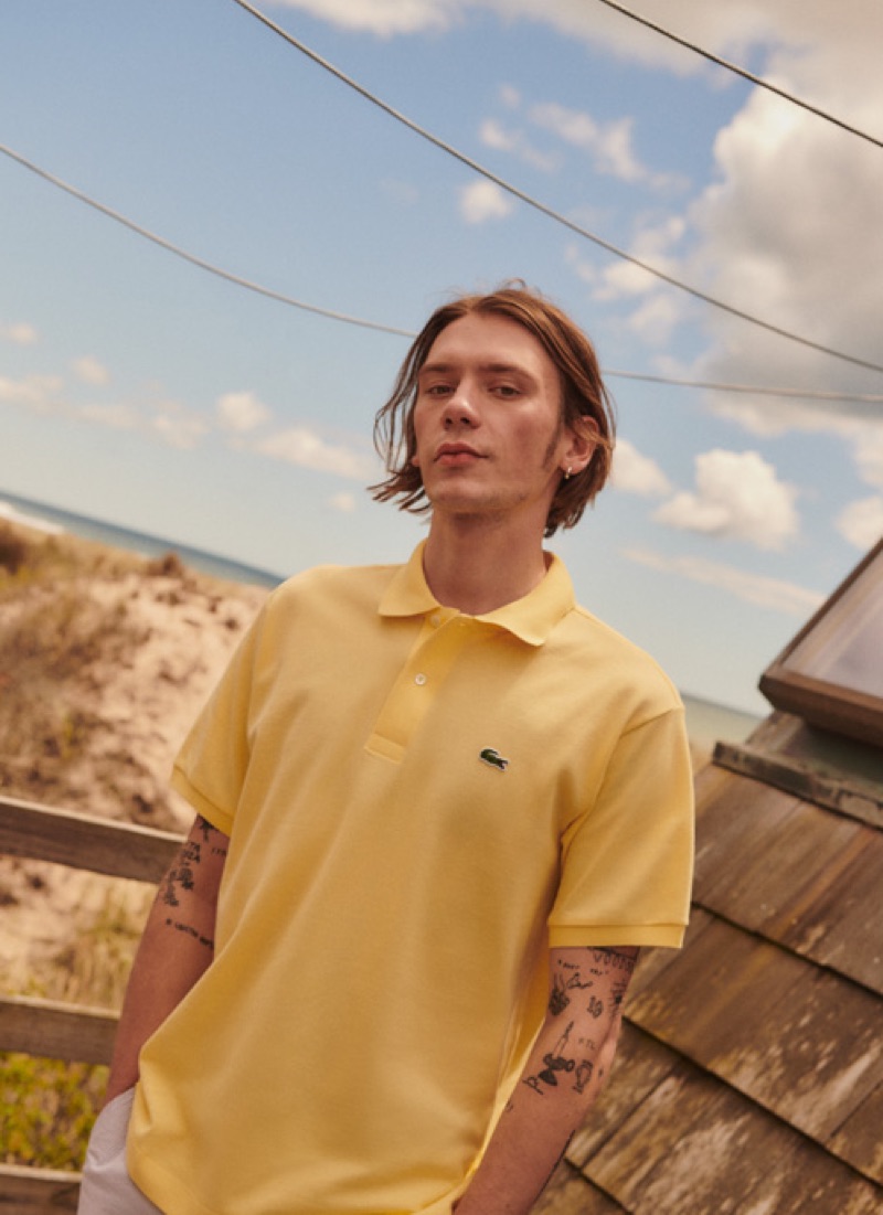 Model Luca Bertea rocks a yellow Lacoste polo with Club Monaco stripe shorts.