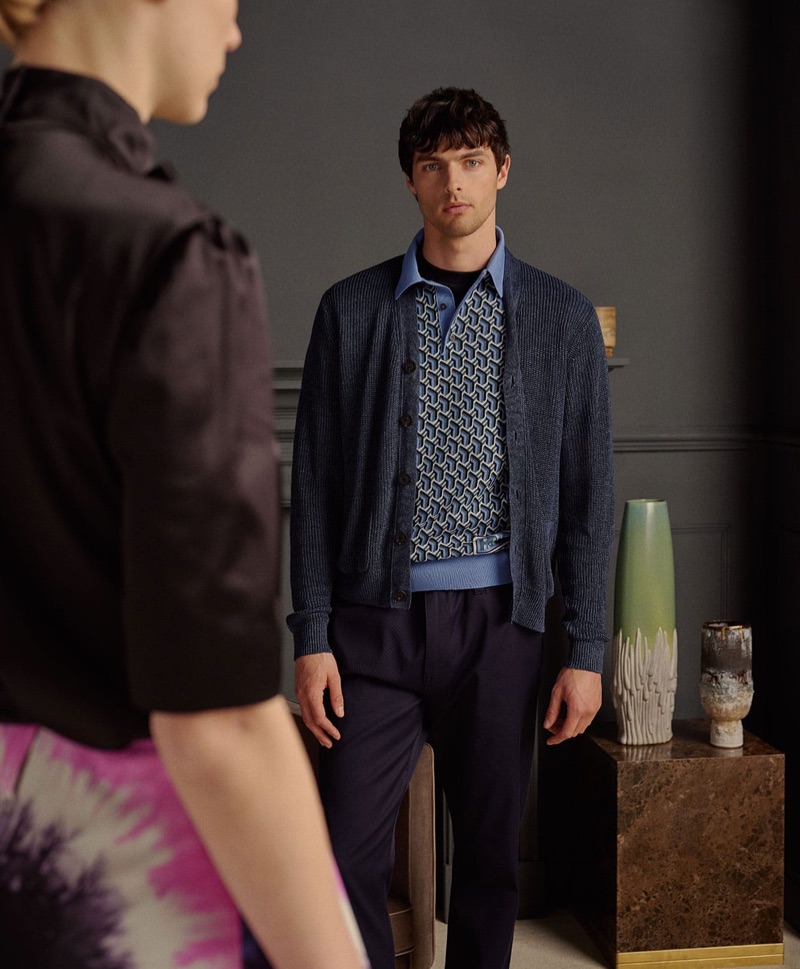 Layering, Hannes Gobeyn models an Iris Von Arnim cardigan with a polo shirt, t-shirt, and trousers by Prada.