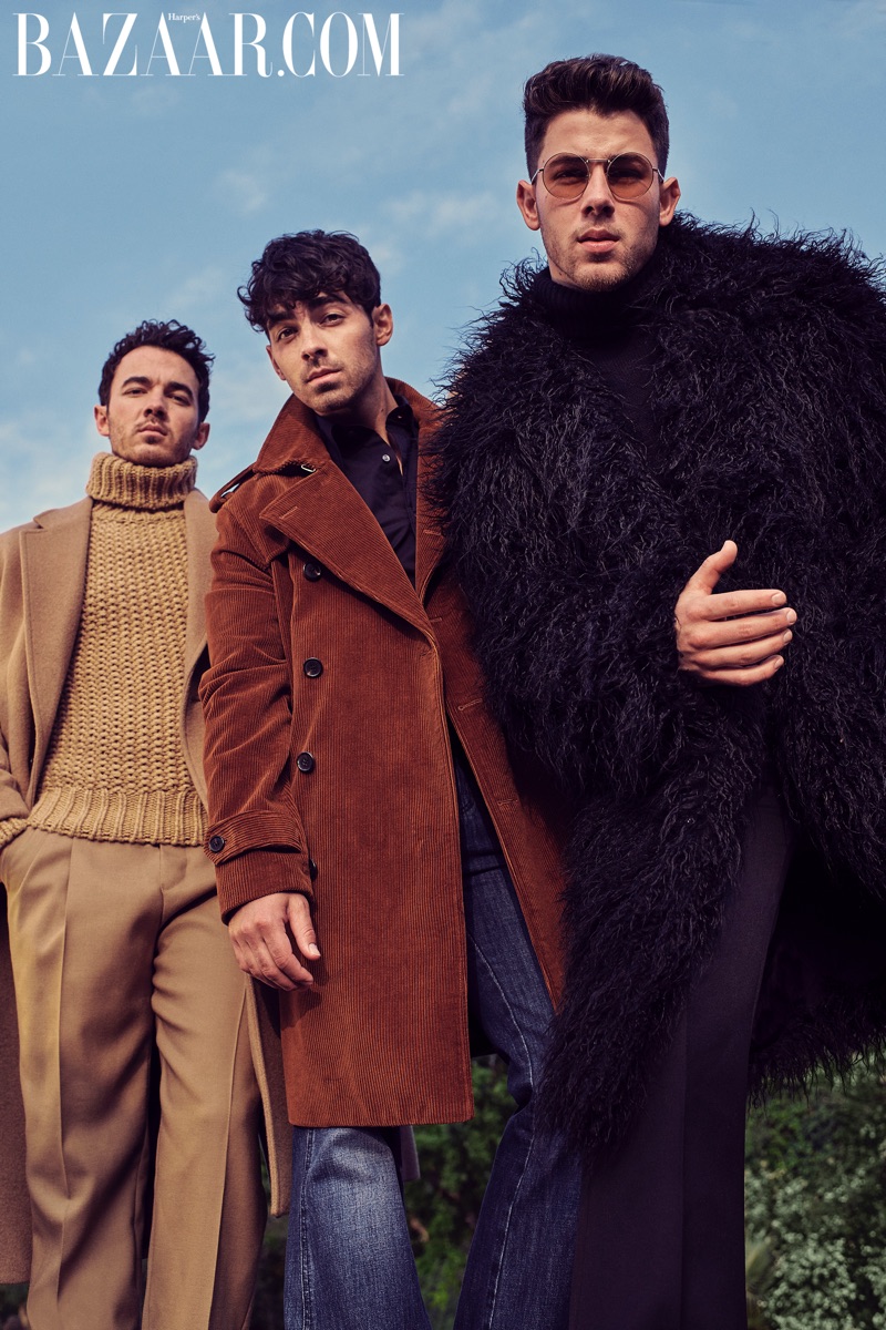 Tapping into retro style, Kevin Jonas wears a Michaels Kors camel coat, turtleneck and pants. Joe Jonas dons a Michael Kors cognac corduroy coat, black shirt and denim jeans. Meanwhile, Nick Jonas wears a  Michael Kors black coat, turtleneck and pants with Valentino sunglasses.