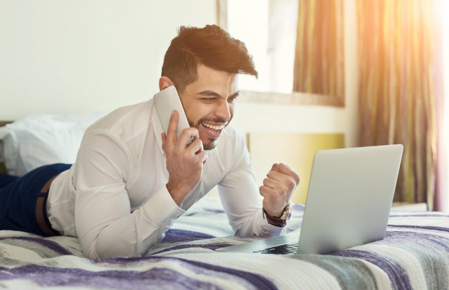 Man on Bed Talking on Phone with Laptop