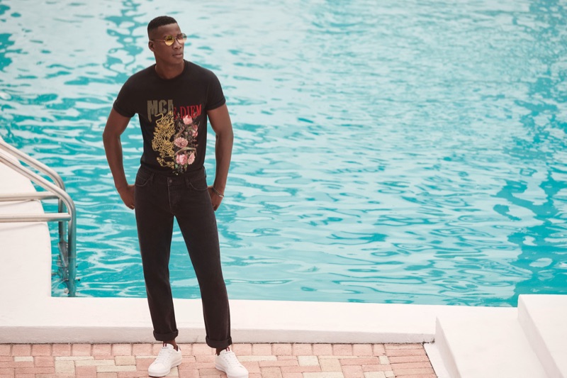 Pictured poolside, David Agbodji rocks a graphic t-shirt with black jeans by River Island.