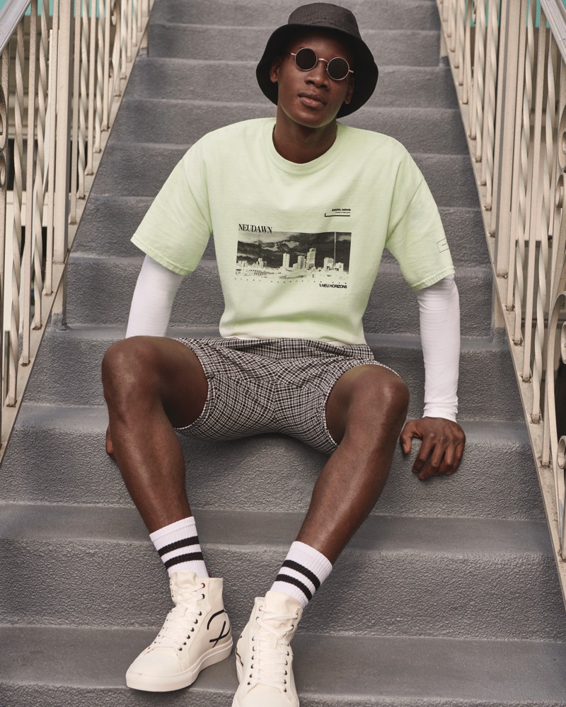 A cool vision, David Agbodji sports a bucket hat, t-shirt, and plaid shorts by River Island.