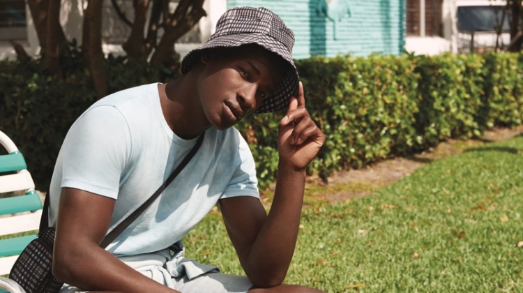 Connecting with River Island, David Agobdji sports a summer look, complete with a plaid bag and bucket hat.
