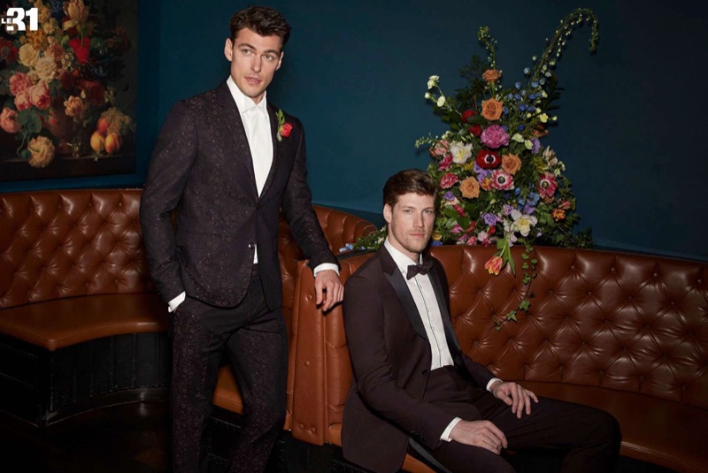 Dressed to impress, Filip Wolfe and Alex Loomans charm in sharp looks from Simons. Left: Filip dons an iridescent burgundy floral jacquard suit with a white shirt by LE 31. Right: Alex wears a burgundy tuxedo with a piped shirt and bow-tie by LE 31.