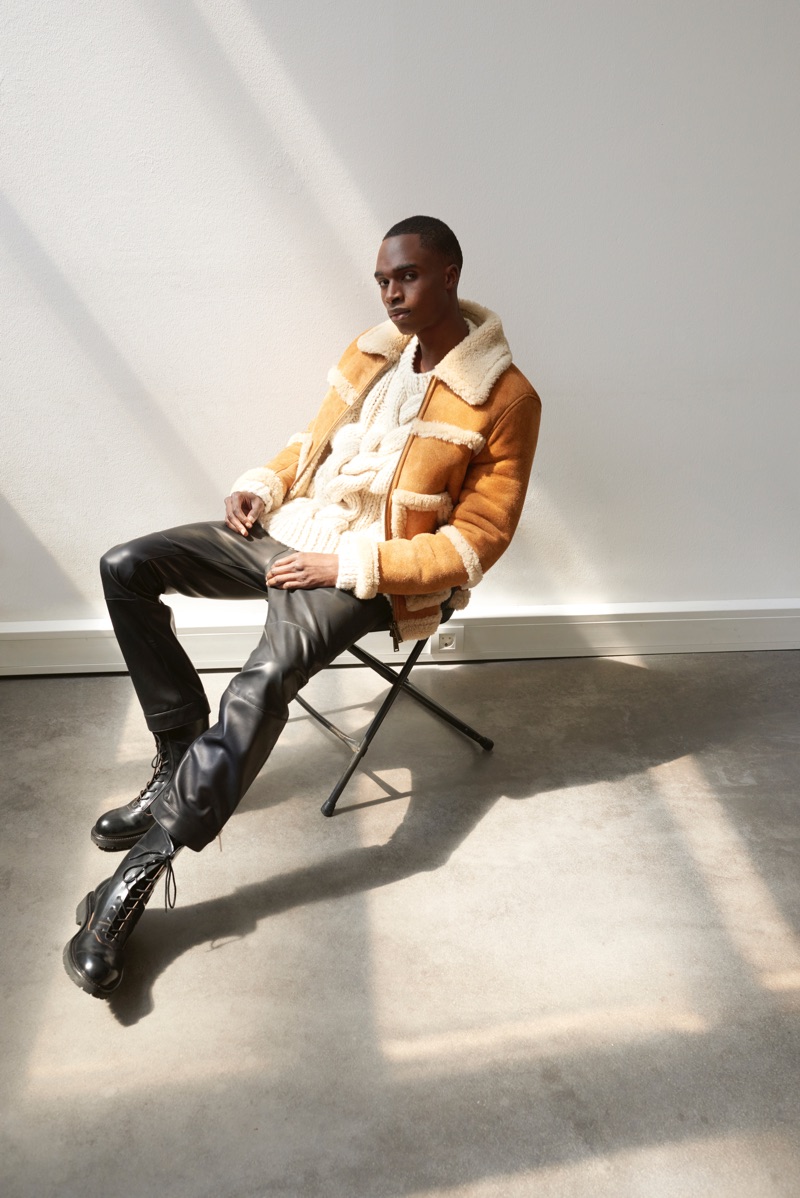 Retreating indoors, Bakay Diaby dons a shearling jacket, sweaters, and pants by Dsquared2. Off-White boots complete his look.