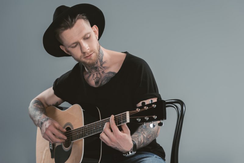 Male Model Tattoos Wearing Hat Playing Guitar