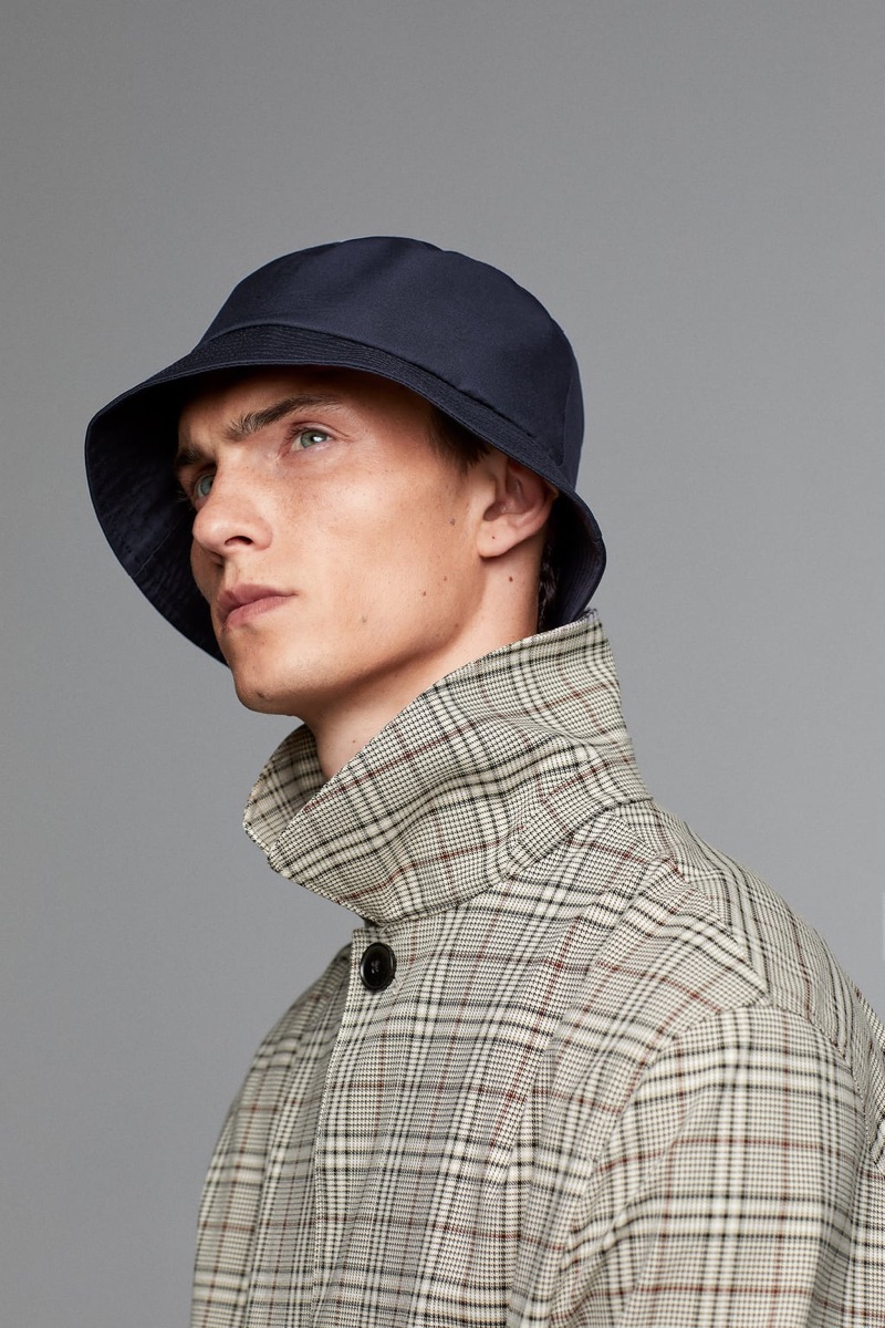 French model Luc Defont-Saviard dons a bucket hat and checked coat from Zara Man's traveler collection.