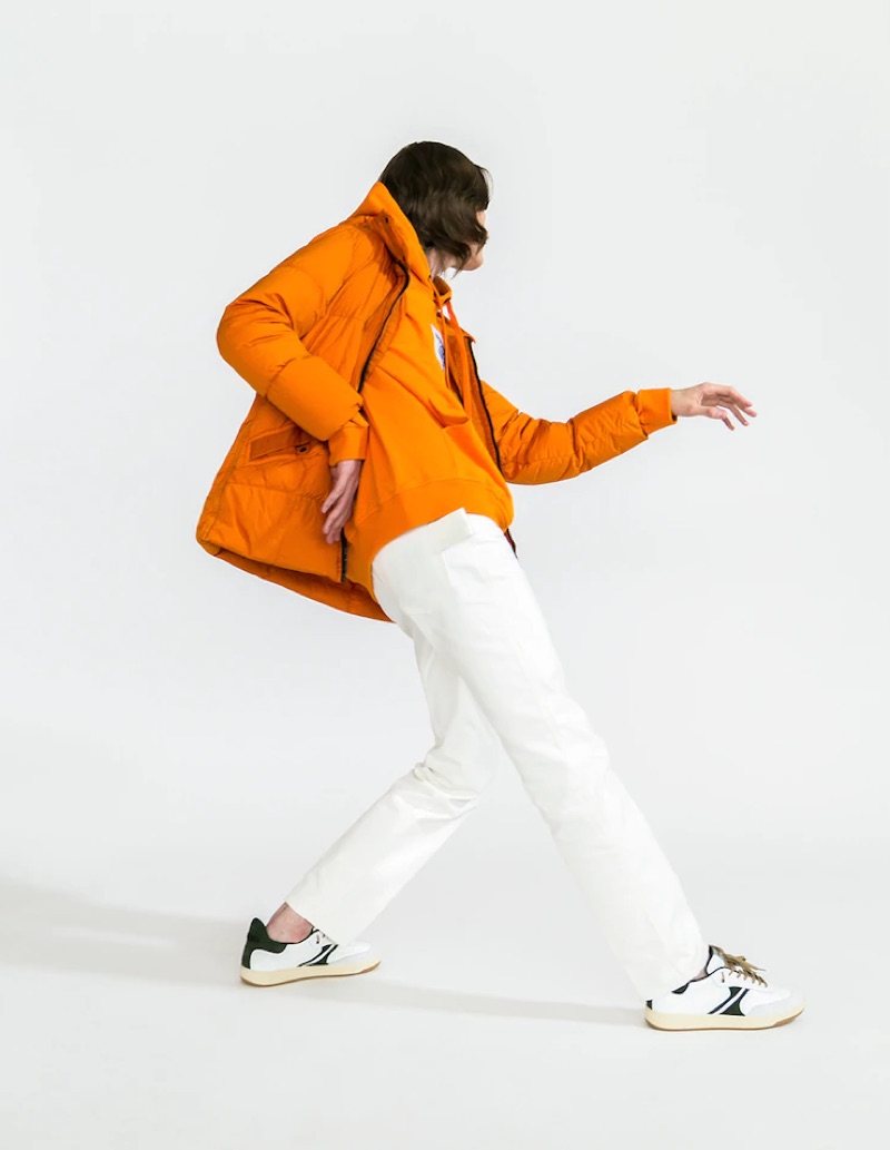 Striking a pose, Alex Rychkov dons an orange Stone Island nylon puffer jacket $998, Burberry hoodie $590, white Moncler Genius pants $440, and AM318 sneakers $217.