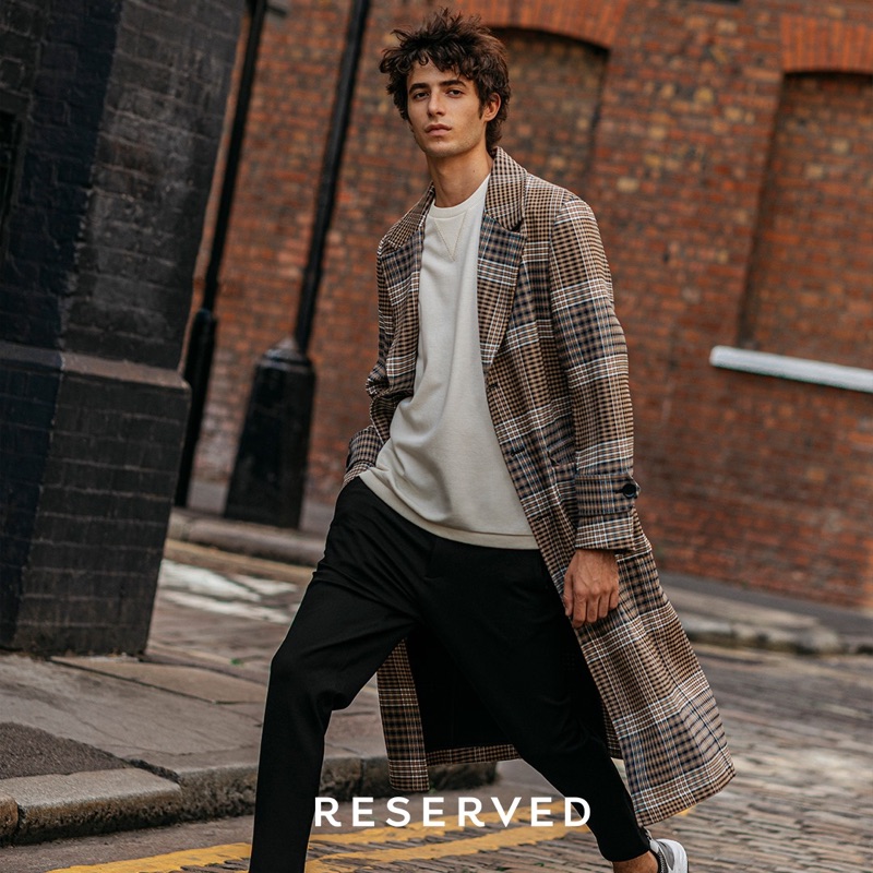 On the move, Oscar Kindelan wears a Reserved checked coat with a sweatshirt and trousers. 