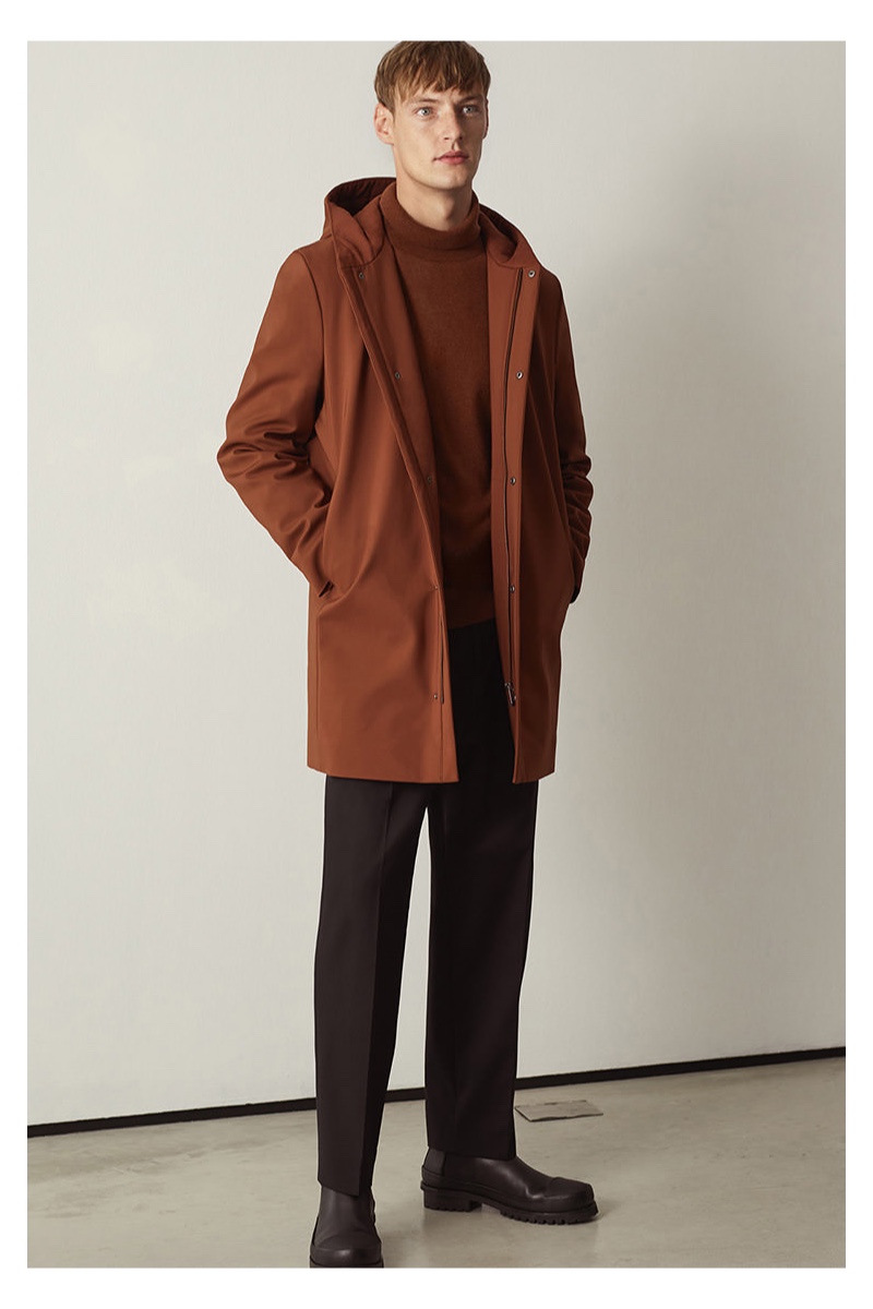 Embracing autumnal tones, Roberto Sipos models a hooded coat with a sweater and trousers by COS.