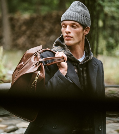 Rocky Harwood sports a Coach 1941 hoodie, Billy Reid peacoat, A.P.C. Petit Standard jeans, a Lotuff leather duffel travel bag, and Barbour beanie.