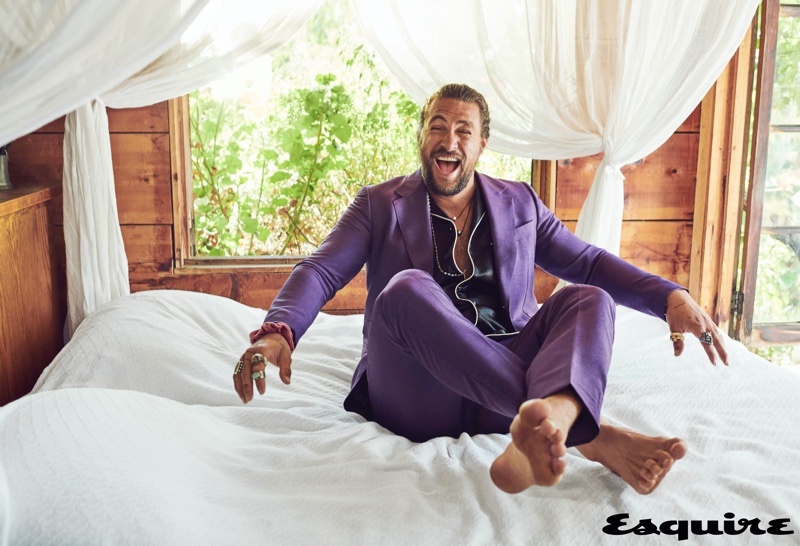 All smiles, Jason Momoa wears a shirt and purple suit by Gucci. His accessories put the spotlight on Rainbow Gems, Red Rabbit Trading Co., Book of Alchemy, and Leroy's Wooden Tattoos.