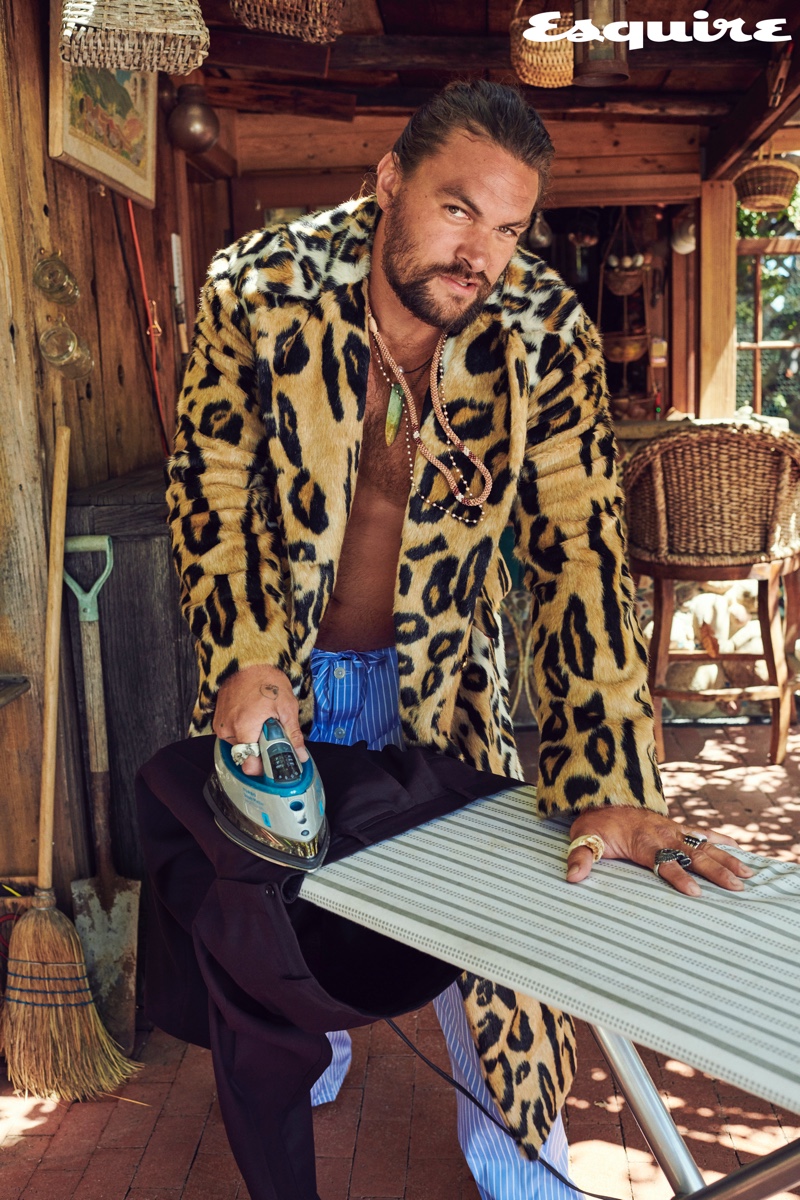 Making a statement in an animal print pattern, Jason Momoa wears a Versace coat. He also wears Paul Stuart pajama pants with necklaces by Rainbow Gems and Red Rabbit Trading Co. His rings come from Book of Alchemy and Leroy's Wooden Tattoos.