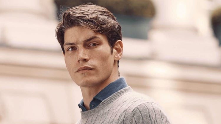 Connecting with Luca Faloni, Sam Way models a light grey cashmere cable knit sweater.