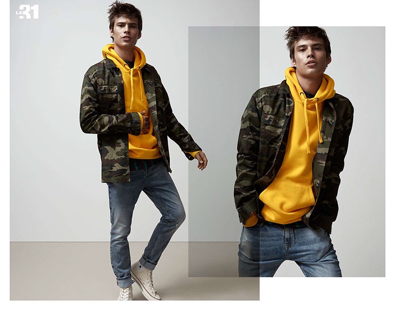 Going casual, Louis Baines wears a LE 31 camouflage print overshirt, yellow hoodie, and slim-fit jeans with Converse Chuck 70 canvas high top sneakers.