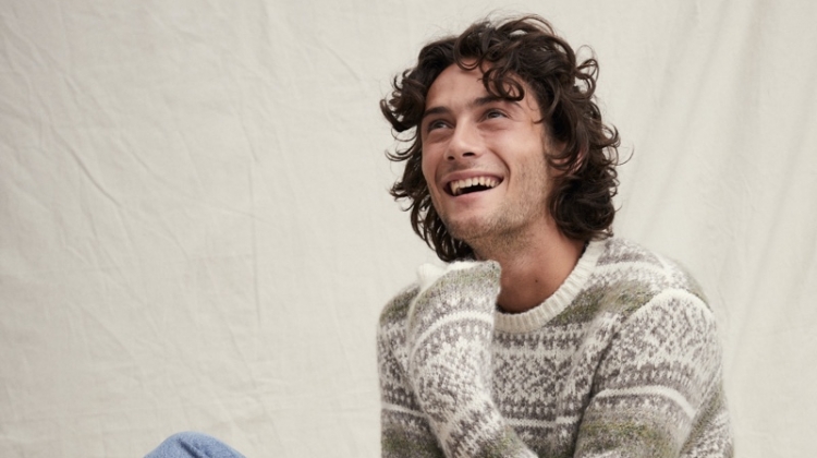 All smiles, Oli Green sports a fairisle sweater with light wash denim jeans from Alex Mill.