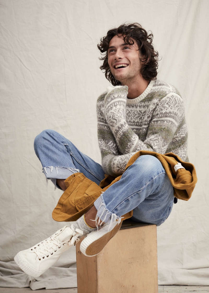 All smiles, Oli Green sports a fairisle sweater with light wash denim jeans from Alex Mill.