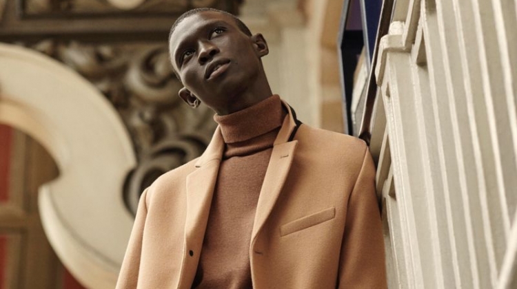 Fernando Cabral dons a camel-colored coat with a brown turtleneck sweater and light wash jeans from H&M.