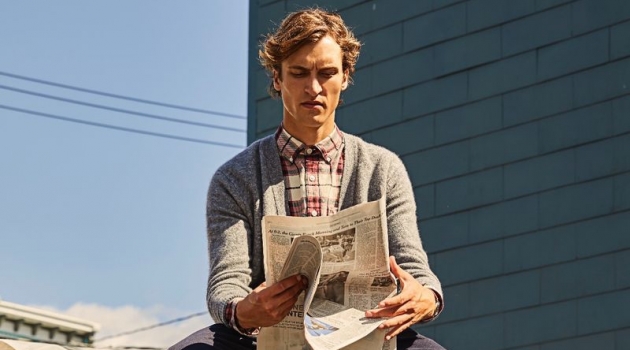 Reading the newspaper, Tim Dibble models a Todd Snyder red plaid flannel shirt $178 and Italian merino cardigan $198.