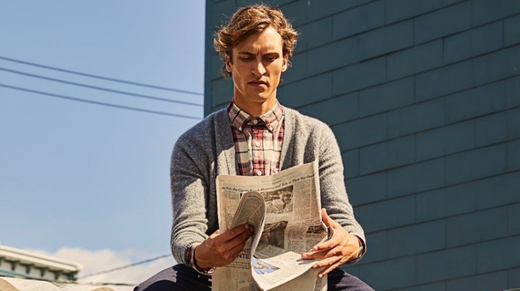 Reading the newspaper, Tim Dibble models a Todd Snyder red plaid flannel shirt $178 and Italian merino cardigan $198.