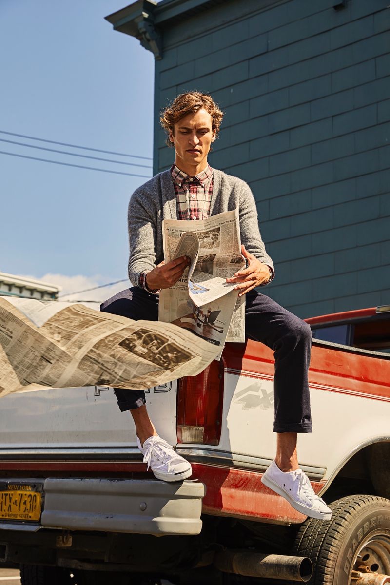 Reading the newspaper, Tim Dibble models a Todd Snyder red plaid flannel shirt $178 and Italian merino cardigan $198.