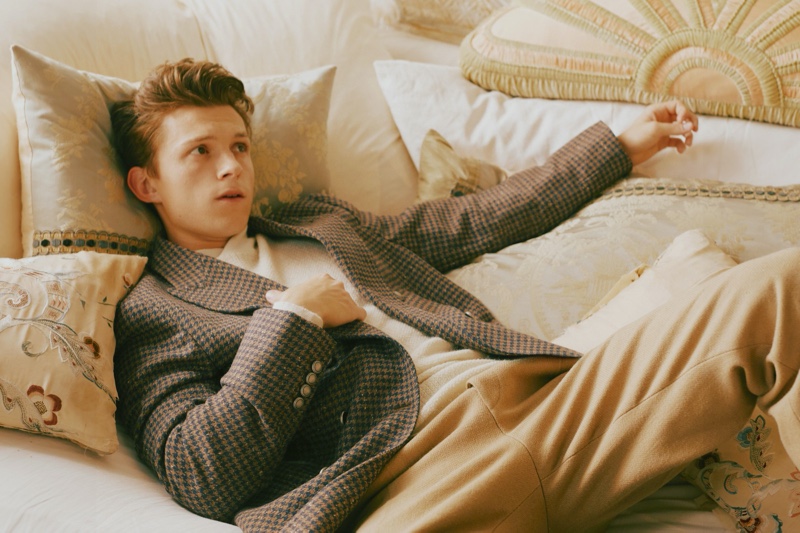 Relaxing, Tom Holland wears a Brunello Cucinelli blazer, Salvatore Ferragamo sweater, and BOSS pants for GQ Style USA.