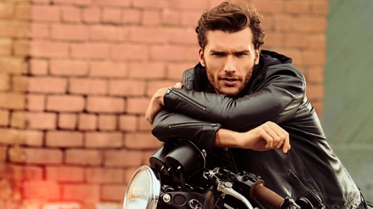 Posing on a motorcycle, Aurelien Muller sports a leather jacket and jeans from IKKS.