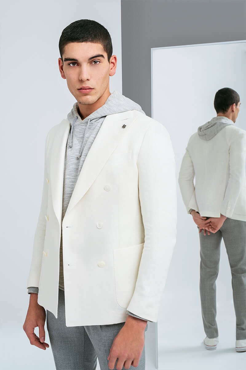 A fresh vision, Samuele Urbani sports a cream double-breasted jacket with a gray marle hoodie and pleated trousers for Lubiam's spring-summer 2020 campaign.