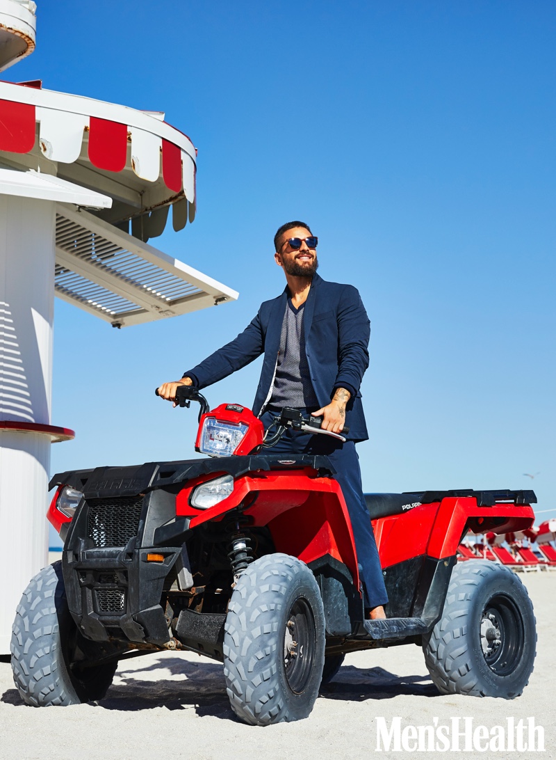 Maluma sports a Calvin Klein suit jacket and pants with a Lands' End sweater. He also sports Persol sunglasses for Men's Health.