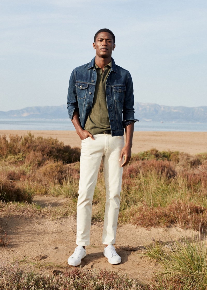 Donning a jean jacket with a smart polo and white pants, Hamid Onifade wears Mango.