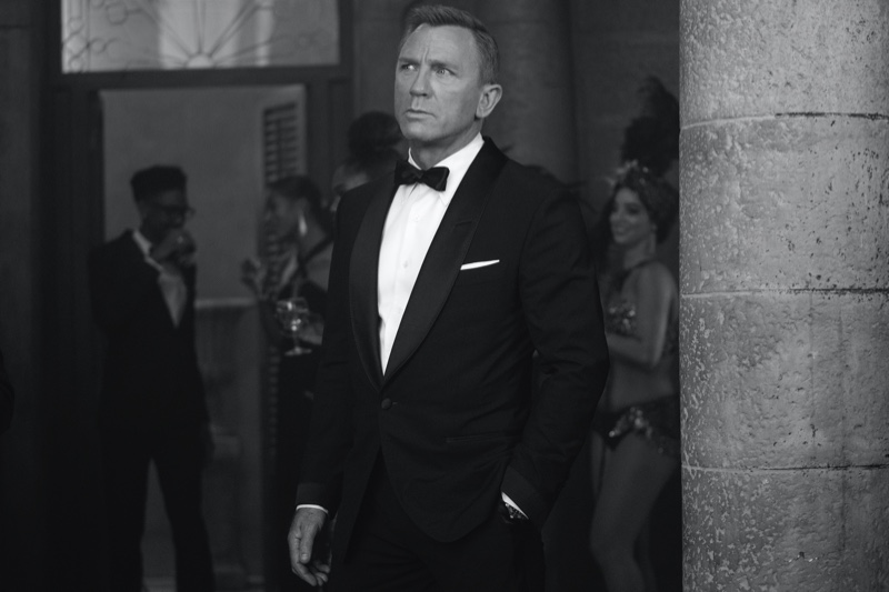 Dressed to impress, Daniel Craig returns as James Bond in No Time to Die. Craig dons a Tom Ford black wool Atticus shawl collar cocktail jacket with quilted satin lapel and cuffs. A dapper vision, Craig wears Tom Ford Atticus evening trousers, a white poplin collared shirt, satin self bowtie, and off white silk pocket square as well. | Photo courtesy of Tom Ford | Photo Credit: Nicola Dove © 2020 Danjaq, LLC, and MGM. All Rights Reserved.