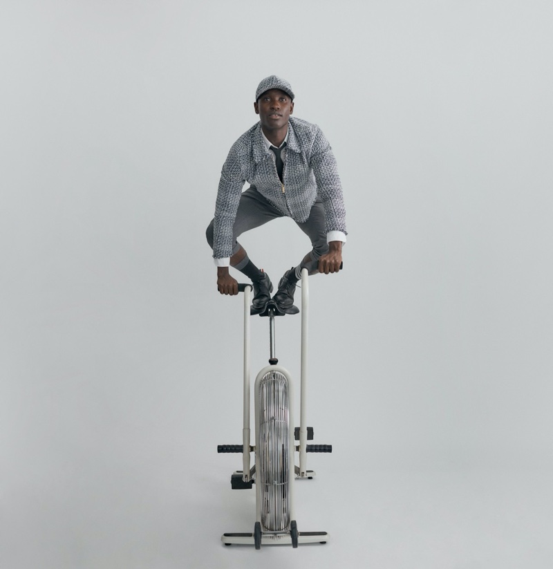 Charles Oduro gets in a workout on an exercise bike as he dons a gray look from the Thom Browne x Nordstrom Concepts 009 collection.