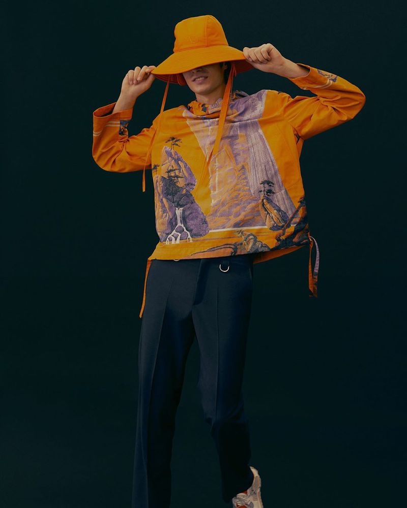 Embracing a graphic pop of color, Oscar Kindelan models a Valentino nylon city-print jacket and technical fabric hat with wool and mohair-blend pants from Mytheresa.