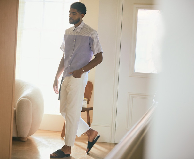 Elijah Fennell wears a Maison Margiela look that includes a striped shirt, 5-pocket pants, a measuring tape belt, pool slides, and an open cuff bracelet.