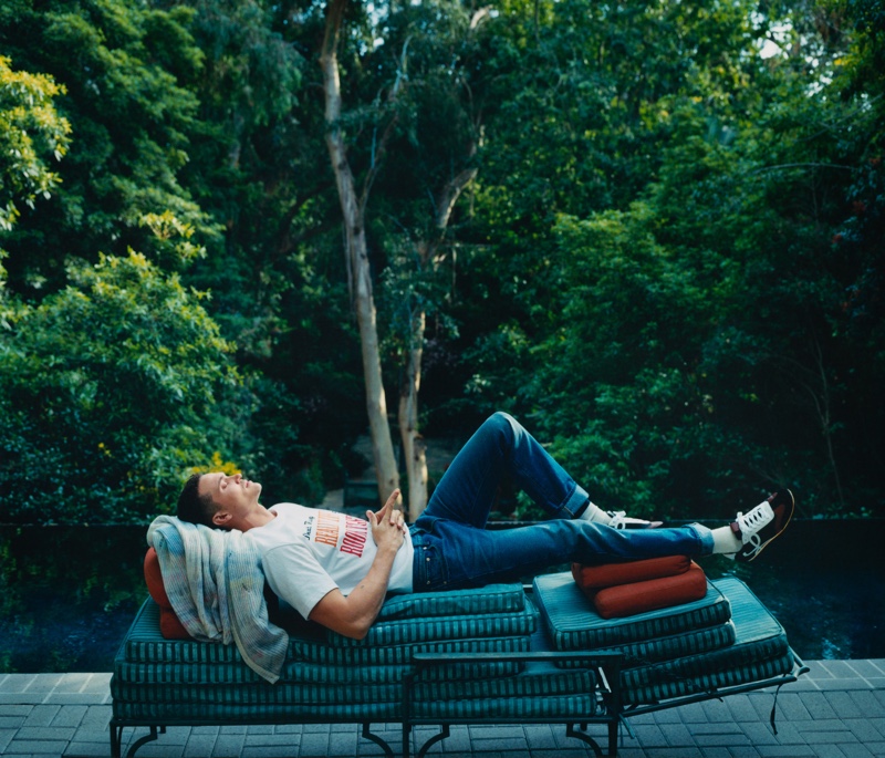 Stealing a moment of relaxation, Karl Glusman wears a Sacai t-shirt, Gucci jeans, and Loewe sneakers.