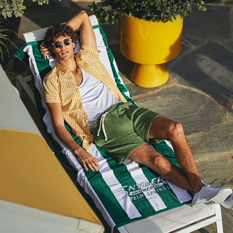 Lounging, Francisco Henriques models a Todd Snyder micro gingham short-sleeve shirt in yellow with Todd Snyder + Champion green lightweight warm up shorts.