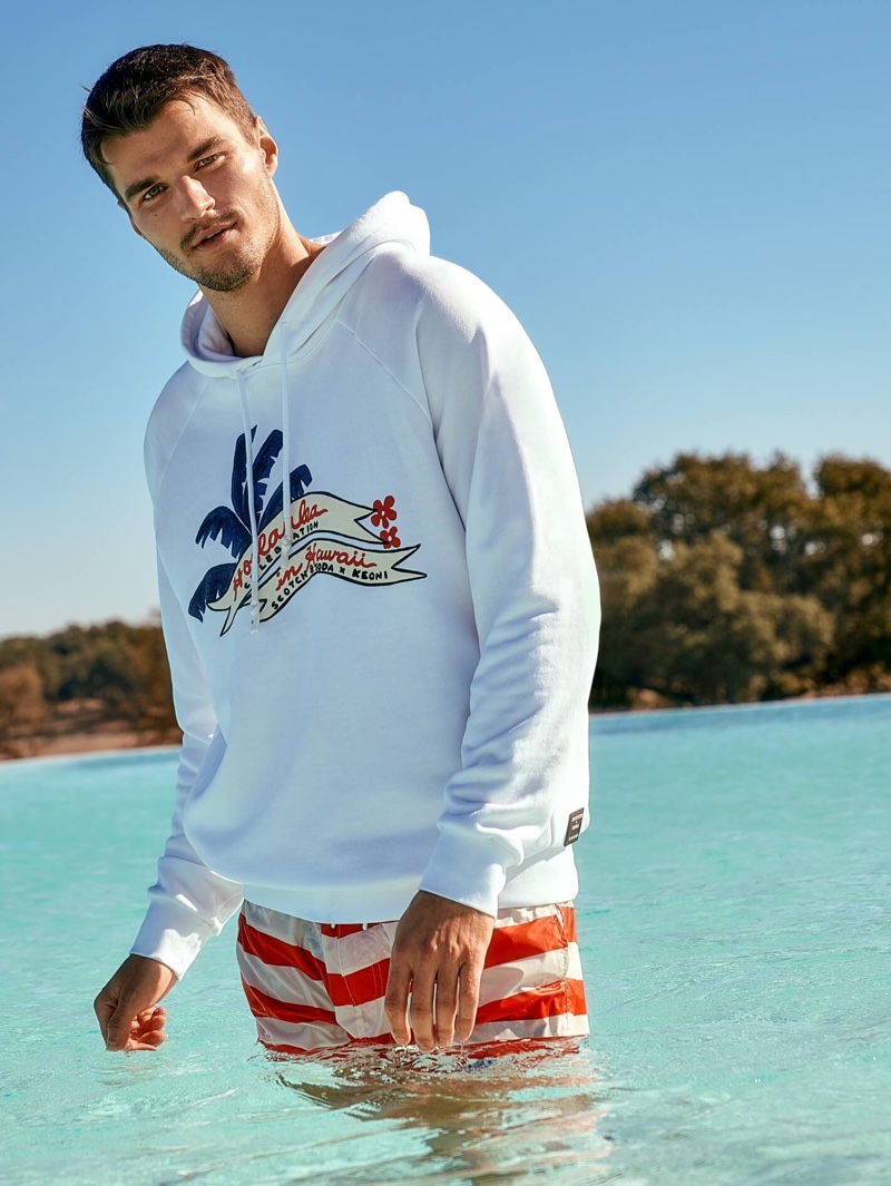 Arran Sly sports an artwork hoodie with mid-length swim shorts from Scotch & Soda's Keoni collection.