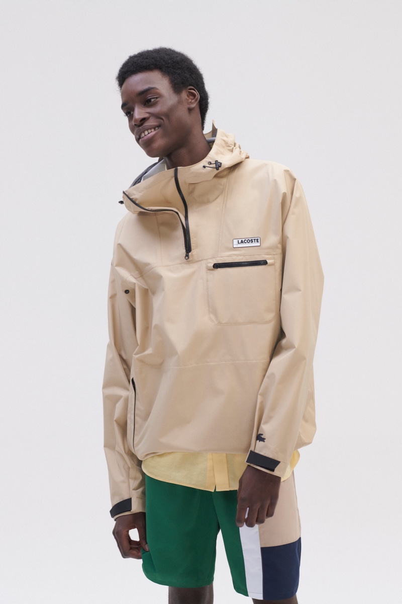 Model Babacar N’doye dons a windbreaker, color-blocked pants, and a yellow shirt from Lacoste.