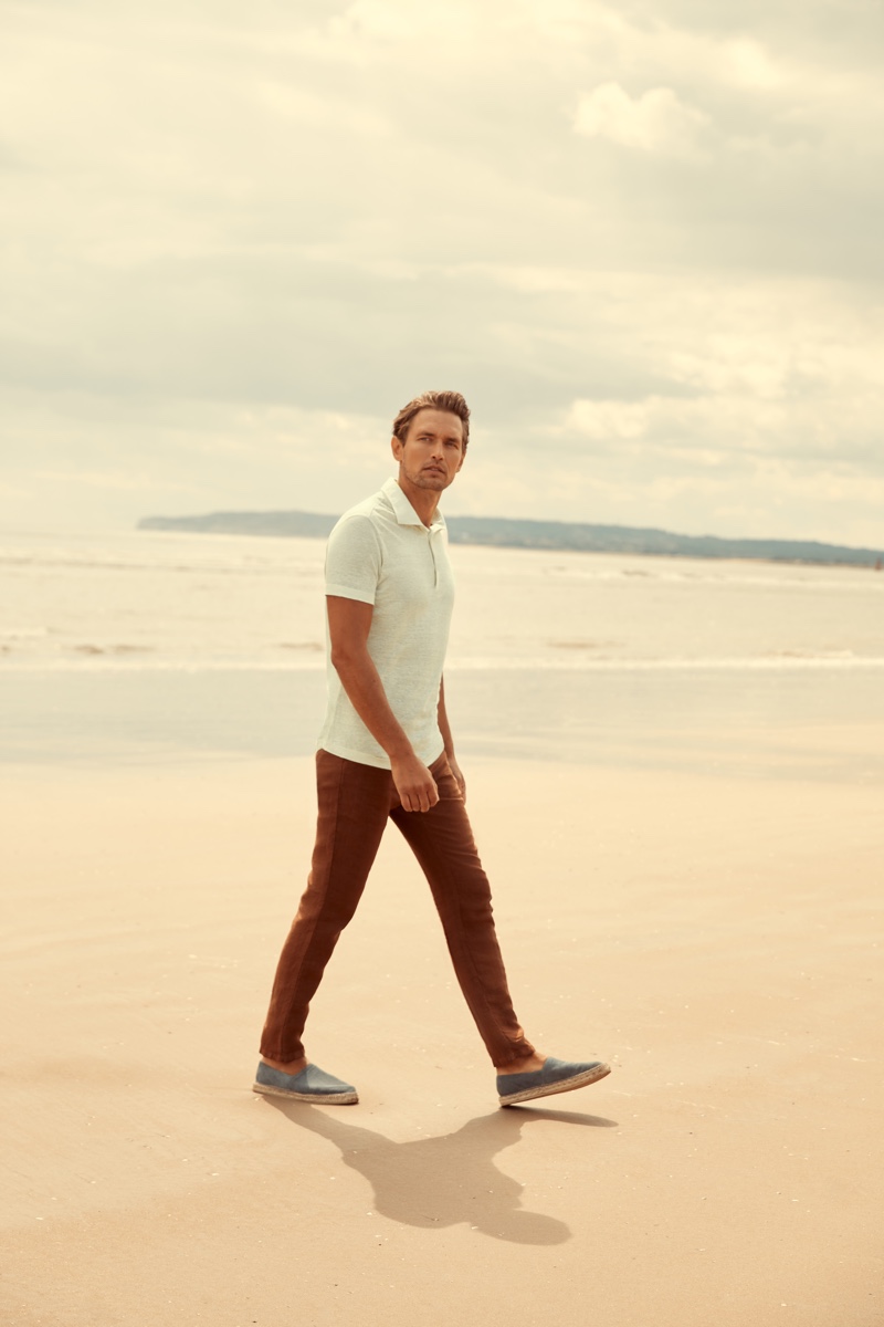 Taking to the beach, Robertas Aukstuolis models Luca Faloni's cream elba linen jersey polo for the label's high summer 2020 campaign.