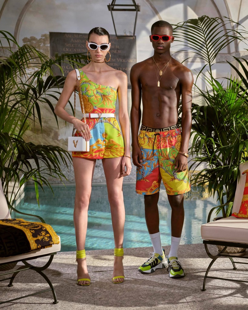 Relaxing poolside, Ismael Savane rocks Versace's summer capsule print swim shorts with cherry red sunglasses.