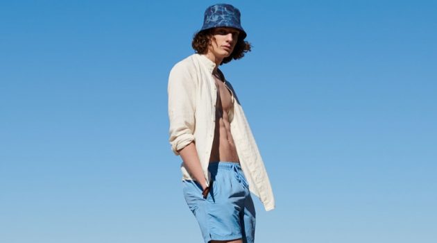 Pawel Hits the Beach with Reserved Sporting a bucket hat with a yellow top and blue swim shorts, Pawel Feledyn wears Reserved.