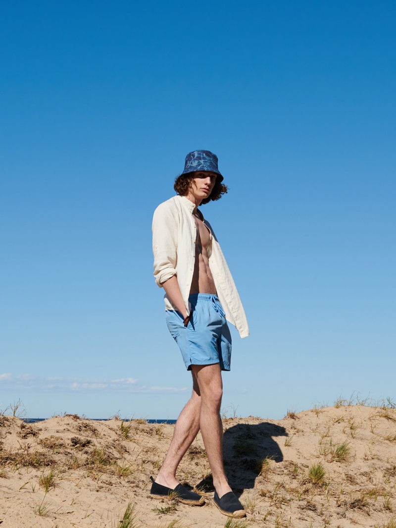 Sporting a bucket hat with a yellow top and blue swim shorts, Pawel Feledyn wears Reserved.