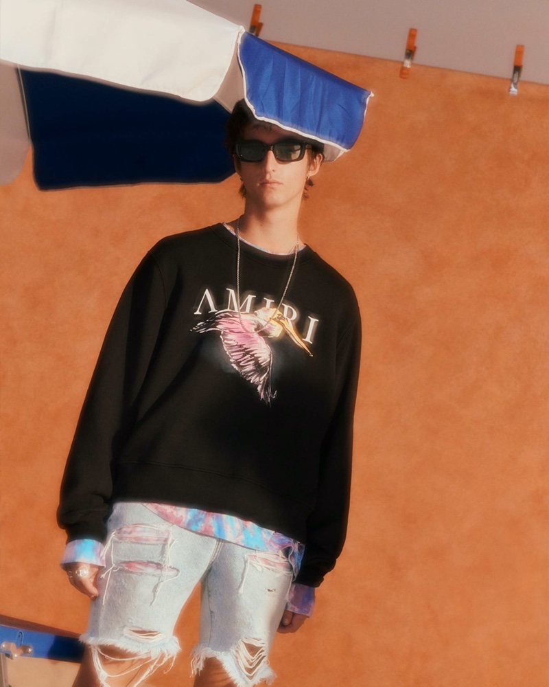 A cool vision, Alexander Carey Morgan wears an AMIRI printed loopback cotton-jersey sweatshirt, tie-dyed cotton-jersey t-shirt, and thrasher paneled distressed denim shorts.