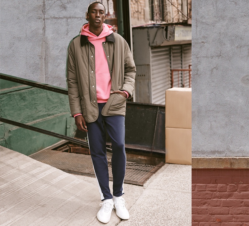 Pop of Color: East Dane suggests switching up the mundane with an easy pairing of comfortable basics and a splash of color. Front and center, model Macky Dabo dons an Adidas x Pharrell Williams Basics hoodie with POLO Ralph Lauren track pants, a Maison Margiela recycled nylon quilted jacket, and Adidas x Craig Green sneakers.