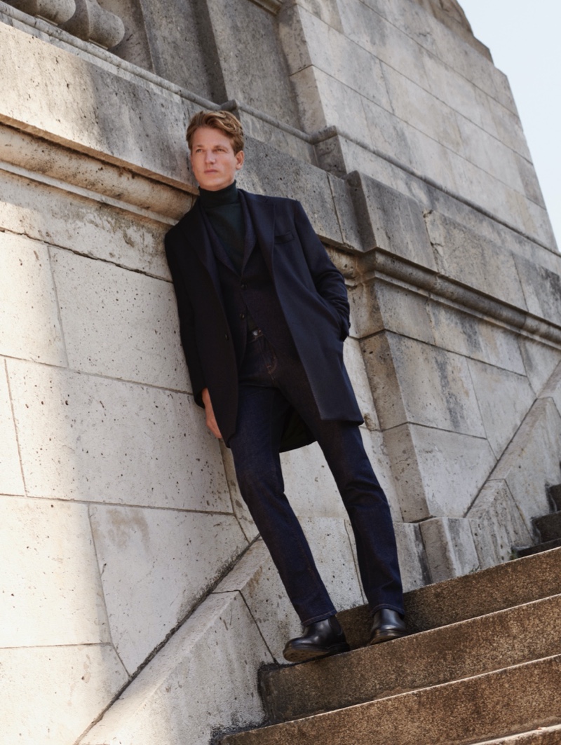 Layering for fall, Hugo Sauzay dons a sleek coat, suit jacket, turtleneck, and jeans from Massimo Dutti.