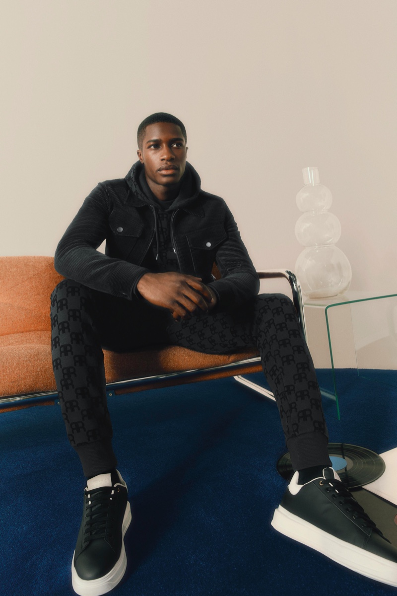 James Kakonge sports a corduroy jacket with a matching RR monogram set and sneakers from River Island's Partywear collection.