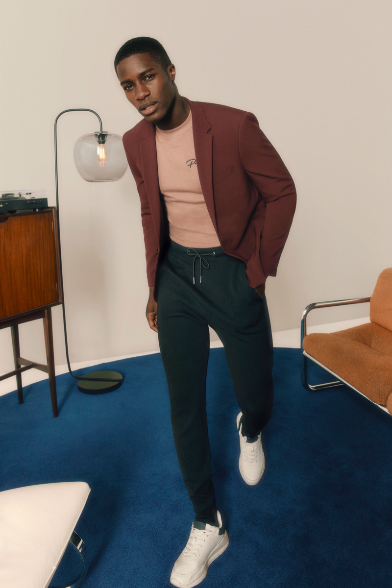 Donning a burgundy blazer, James Kakonge also wears trousers with an elasticated waist from River Island's Partywear collection.
